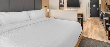A modern hotel room with a large bed, a desk, a flat-screen TV, and a kitchenette.