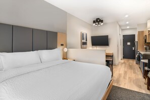 A modern hotel room with a large bed, a desk, a flat-screen TV, and a kitchenette. - XStay Suites Mansfield (Mansfield)