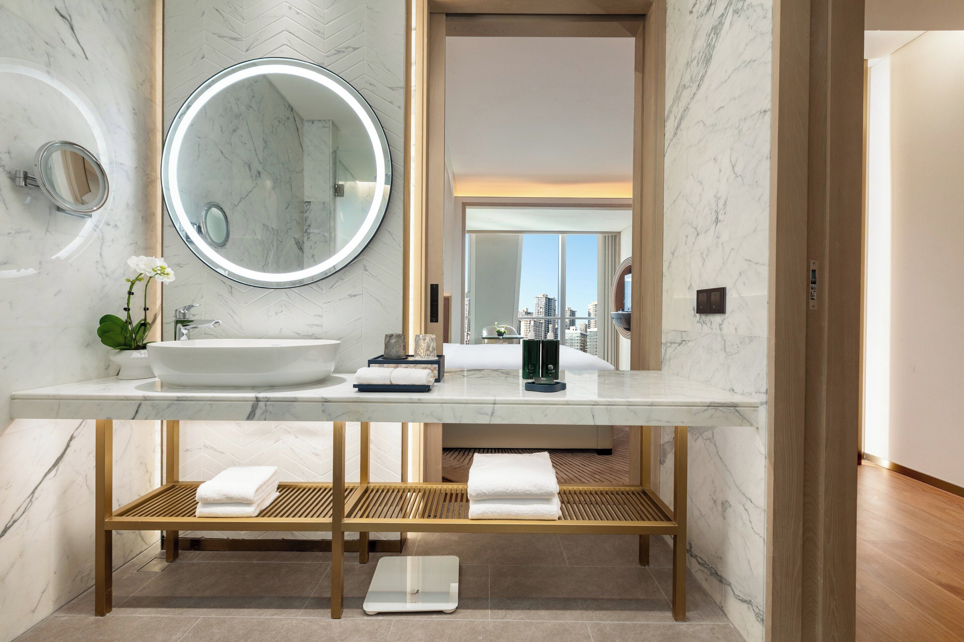 Une salle de bain moderne avec un lavabo en marbre, un miroir rond et un banc en bois.