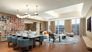A modern living room with a dining area, large windows, a flat-screen TV, and a city view. - Hotel Indigo Zhuhai Hengqin by IHG (Zhuhai)