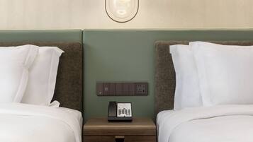 Ett hotellrum med två sängar, ett nattduksbord med en telefon och en väggmonterad lampa.