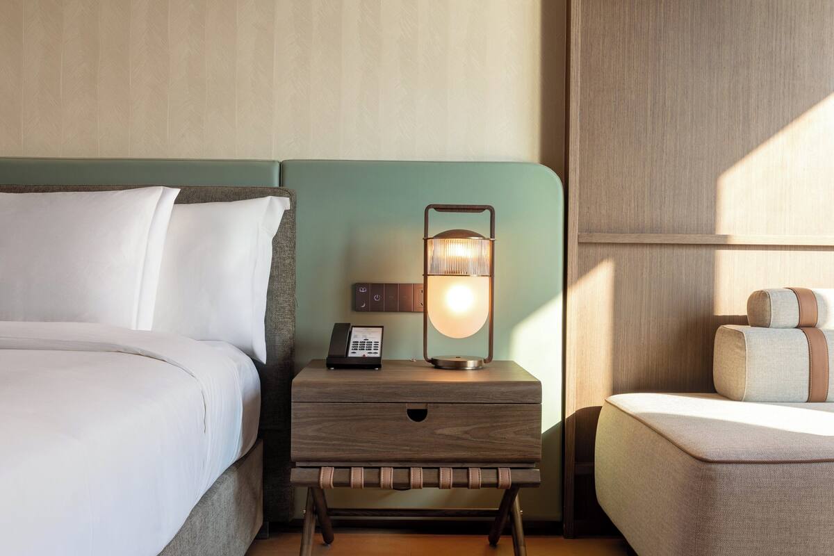 A neatly made bed with white linens, a bedside table with a lamp, and a small nightstand with a phone.