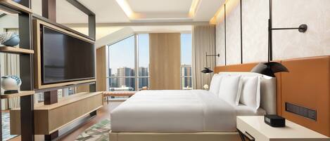 A modern hotel room with a large bed, a flat-screen TV, a bedside table, a bookshelf, and a city view.