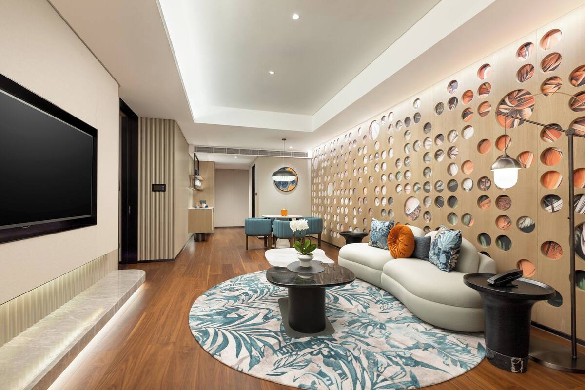 A modern living room with a flat-screen TV, a round coffee table, a sofa, and a dining area with blue chairs.