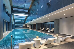 A modern indoor swimming pool with lounge chairs and a glass ceiling. - Hotel Indigo Zhuhai Hengqin by IHG (Zhuhai)