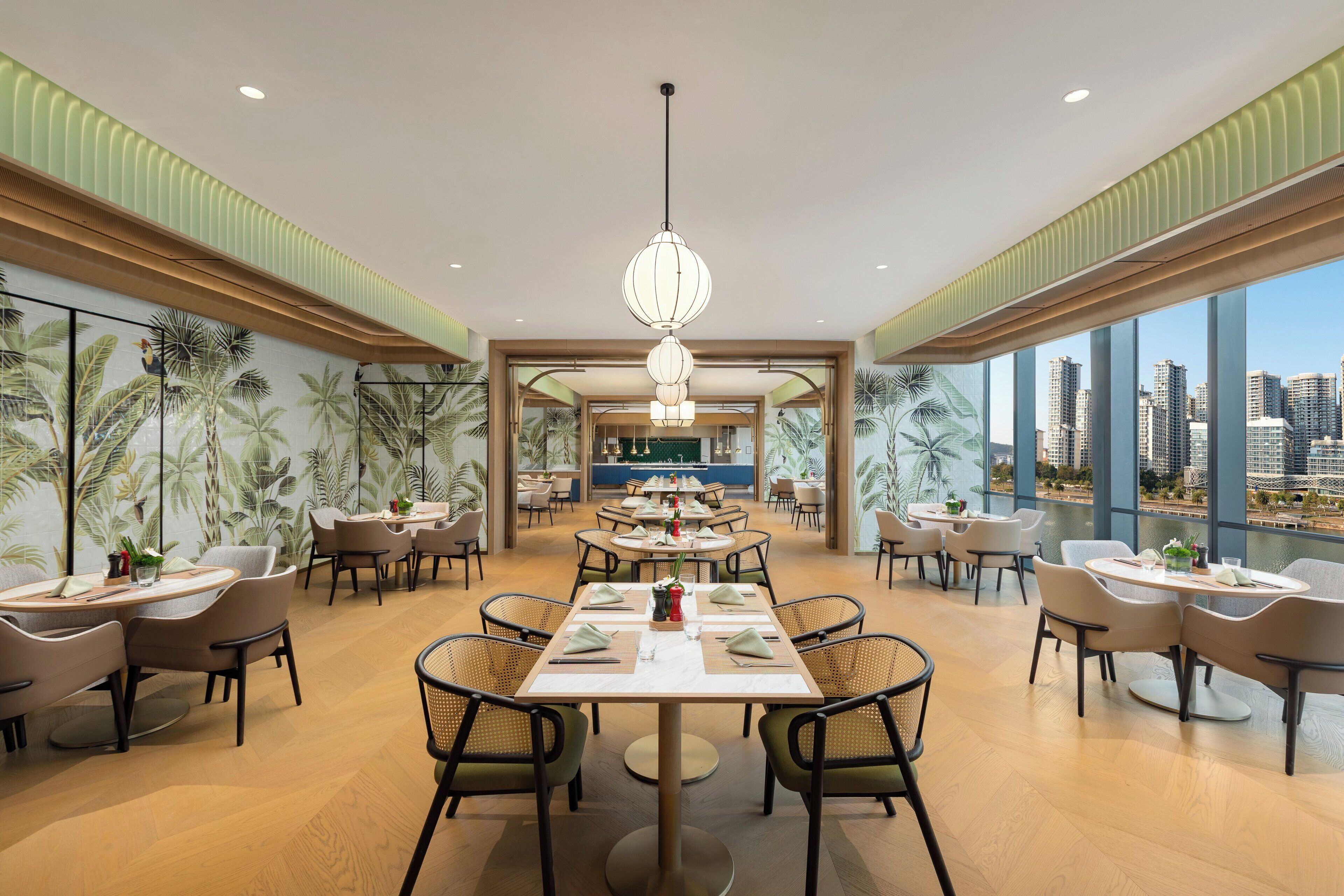 Un vaste espace dédié à la salle à manger, avec de nombreuses tables et chaises, de grandes fenêtres offrant une vue sur la ville et un lustre moderne.