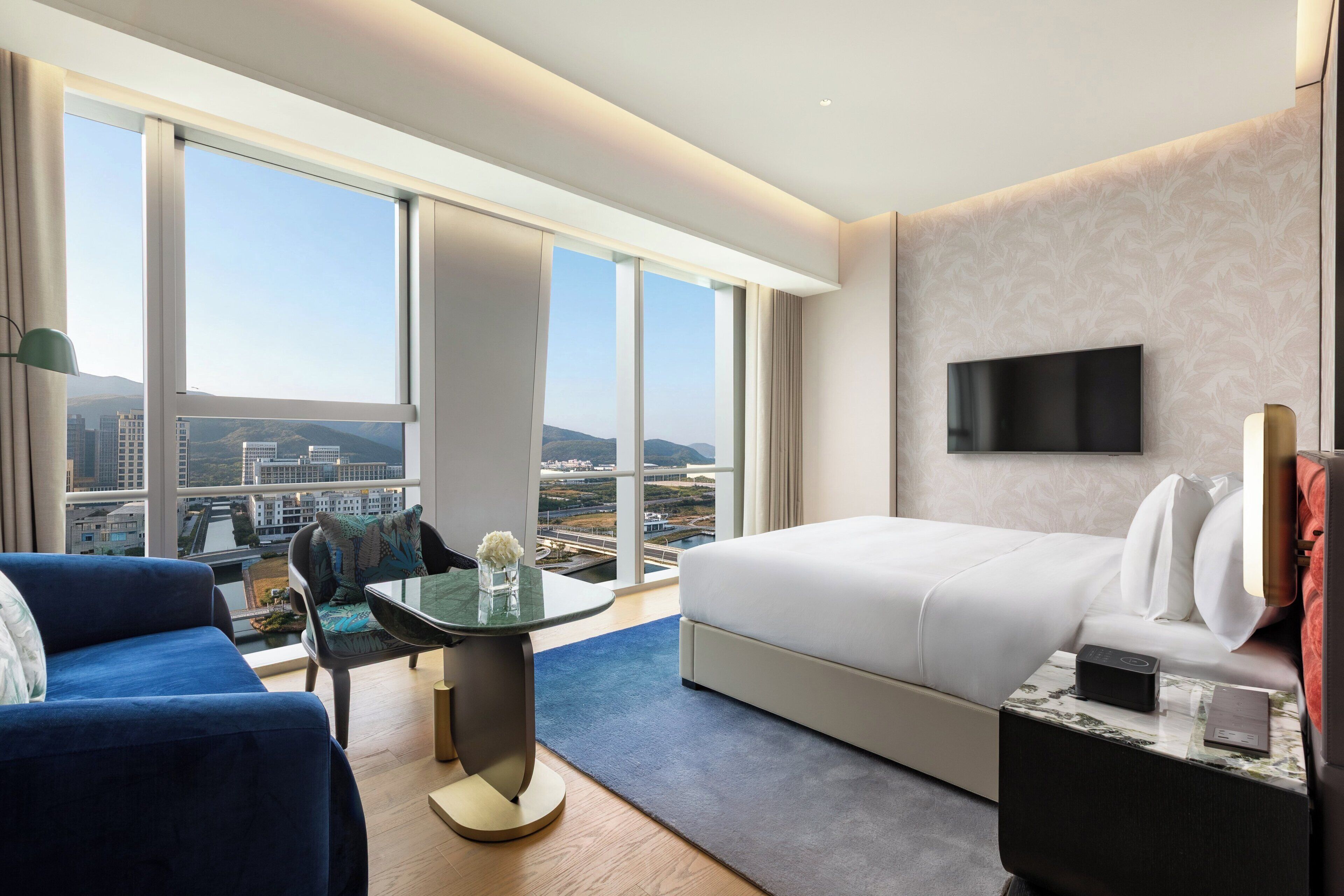 Habitación de hotel moderna con una cama grande, un televisor de pantalla plana, una mesa de comedor y vistas a la ciudad.