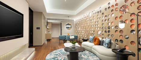 A modern living room with a flat-screen TV, a round coffee table, a sofa, and a dining area with blue chairs.