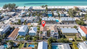 Ett flygbildsbild av ett bostadsområde vid kusten med en strand, hus och en swimmingpool.