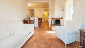 Una sala de estar con sofá, sillón y chimenea. Se ve una escalera que conduce a otra habitación.