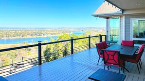 Terraza de madera con una mesa y sillas, con vistas a un lago y un paisaje urbano.