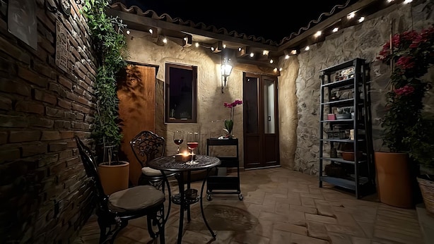 Um pátio externo acolhedor com parede de tijolos, uma mesa com cadeiras e um aparador com plantas.