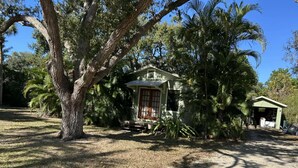 Une maison à deux étages avec un porche, entourée d’arbres et d’un petit abri de jardin.