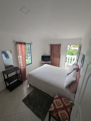 A bedroom with a bed, a TV, a small table, and a window with curtains.