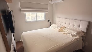 Ein Schlafzimmer mit Bett, Fenster, Klimaanlage und Schreibtisch mit Computer.
