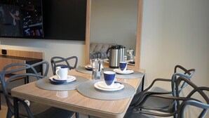 Ein Essbereich mit Holztisch, blau-weißen Tassen, einer silbernen Kaffeekanne und einem an der Wand befestigten Fernseher.