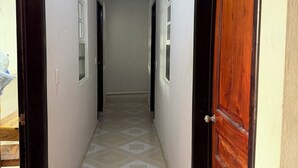A hallway with patterned floor tiles, a wooden door on the right, and a light fixture on the left.