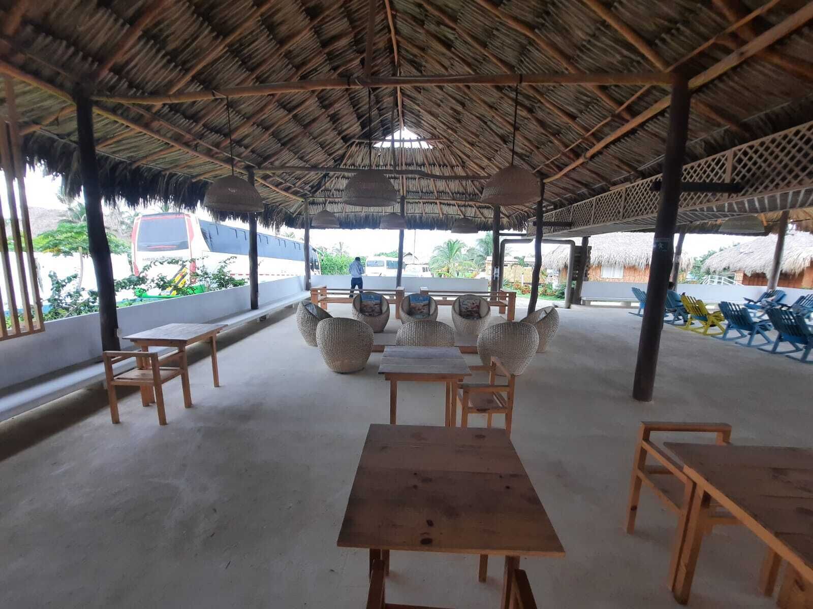 An outdoor seating area with wooden tables and chairs, a thatched roof, and a view of the surrounding landscape.