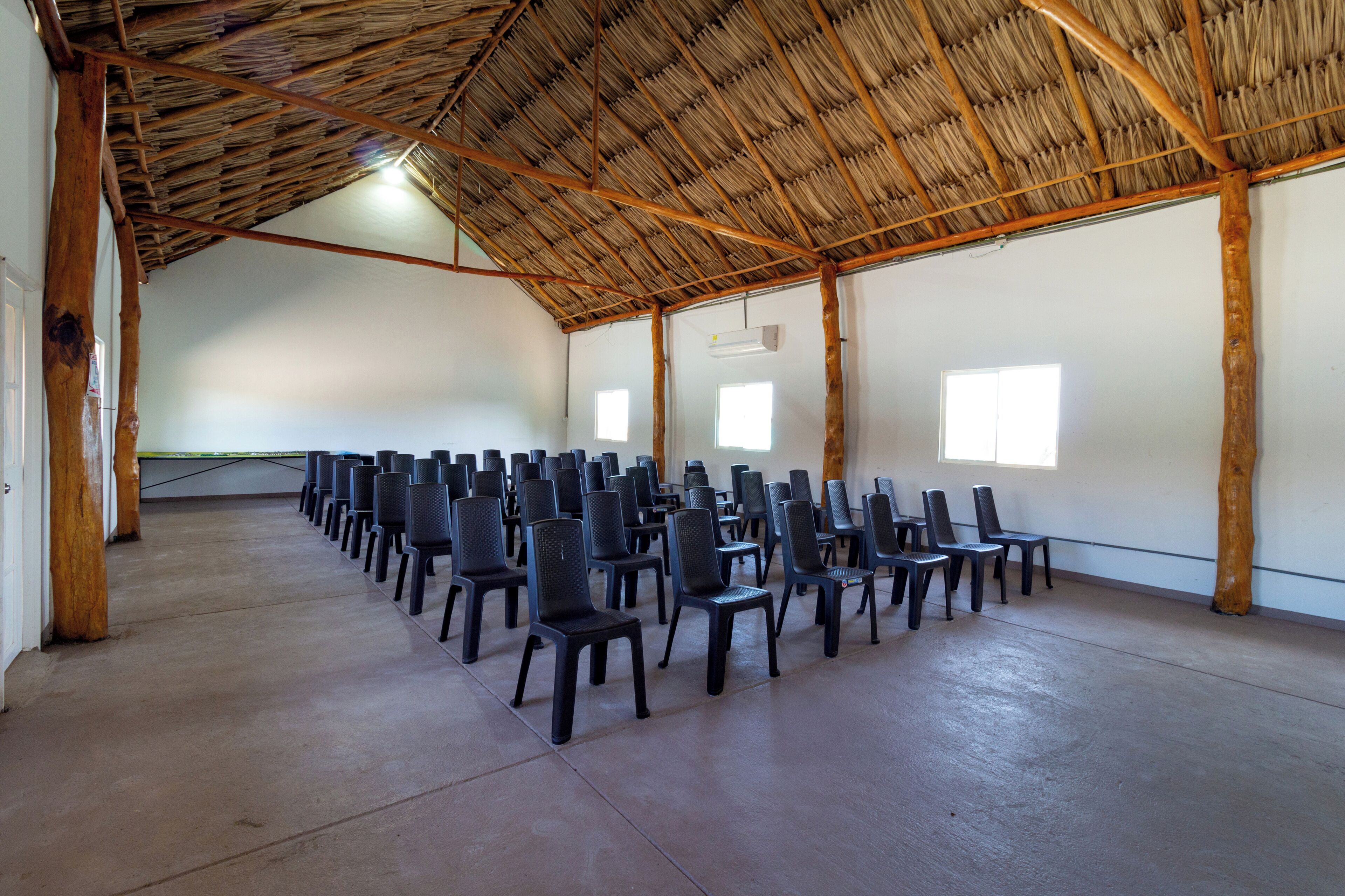A large hall with a thatched roof, rows of black chairs, and white walls.