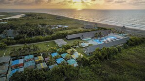 Vista aérea de un resort con edificios de techo de paja, piscina y vista a la playa.