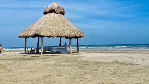 Una cabaña en la playa con techo de paja, una mesa y sillas debajo.