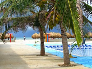 Ein Strand mit Palmen, einem Pool und einer Struktur mit Reetdach.
