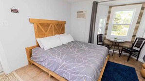 A bedroom with a bed, a small table, a chair, and a window. - Great for couples - The Riverview Suite (Reidville)
