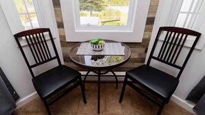 A dining area with two black chairs and a round table, a bowl of green vegetables, and a patterned placemat. - Great for couples - The Riverview Suite (Reidville)