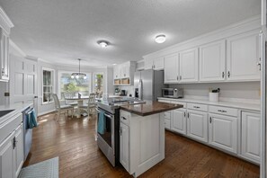 A kitchen with white cabinets, a central island, stainless steel appliances, and a dining area with a table and chairs.