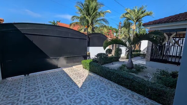 Un ingresso con cancello, un patio piastrellato, palme e un edificio con tetto in tegole rosse.