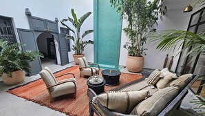 Un espace de détente intérieur, chaleureux et confortable, avec un canapé, des fauteuils et une table basse, agrémenté de plantes en pot et d’une cheminée.