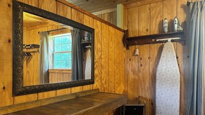 Une salle de bain aux murs lambrissés, dotée d’un grand miroir, d’un porte-serviettes et d’une étagère où sont rangés les articles de toilette.