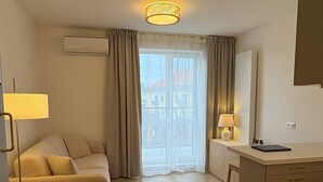 Een moderne hotelkamer met een bank, een klein rond tafeltje, een bureau met een lamp, en uitzicht door een groot raam.