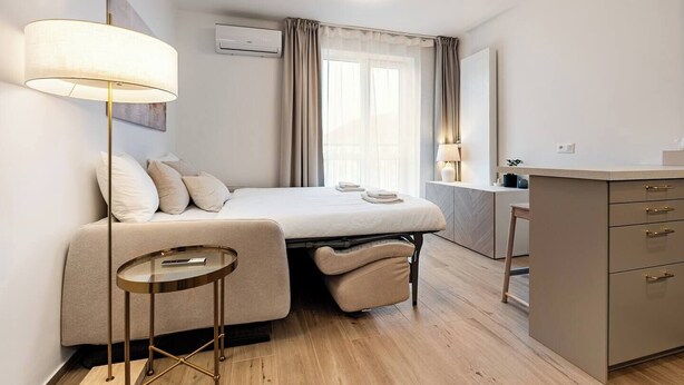 Een moderne hotelkamer met een bed, nachtkastje, lamp, airconditioning en een bureau met lades.