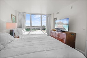 Ein Hotelzimmer mit Bett, Fernseher, Holzkommode und einem großen Fenster mit Meerblick.