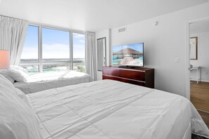 Ein Hotelzimmer mit zwei Betten, einem Fernseher auf einer Holzkommode und einem großen Fenster mit Blick auf die Stadt.