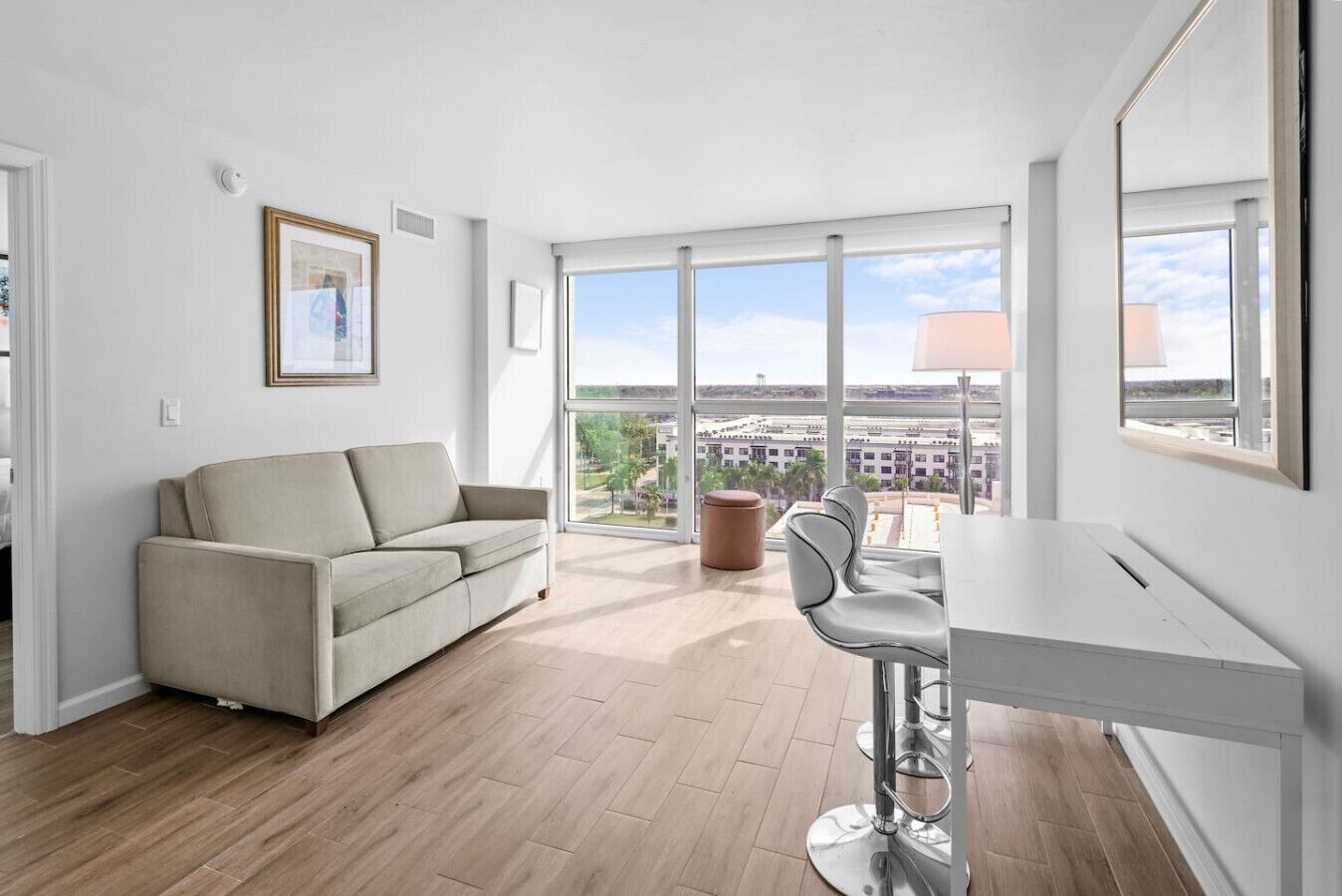 Un appartement moderne doté d’un canapé, d’une table à manger et de chaises, de grandes fenêtres offrant une vue sur la ville et d’un tableau encadré au mur.