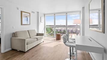 Un appartement moderne doté d’un canapé, d’une table à manger et de chaises, de grandes fenêtres offrant une vue sur la ville et d’un tableau encadré au mur.