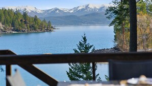A lakeside view with mountains in the background, a wooden deck, and a table with a placemat. - Hughes Hideaway | Lakefront Cabin Near Town (Lakeside)