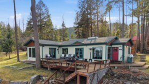 A cabin with a deck, outdoor seating, and a red door. - Hughes Hideaway | Lakefront Cabin Near Town (Lakeside)
