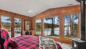 Une chambre avec un grand lit, un mur en bois, une cheminée et une vue sur un lac.