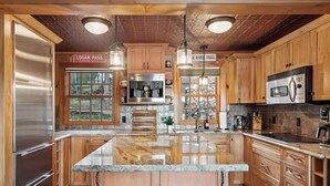 Une cuisine spacieuse avec des meubles en bois, un grand îlot central, des appareils électroménagers en acier inoxydable et un éclairage suspendu.