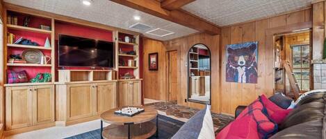 A cozy living room with wooden walls, a large flat-screen TV, and a comfortable seating area with a round coffee table.