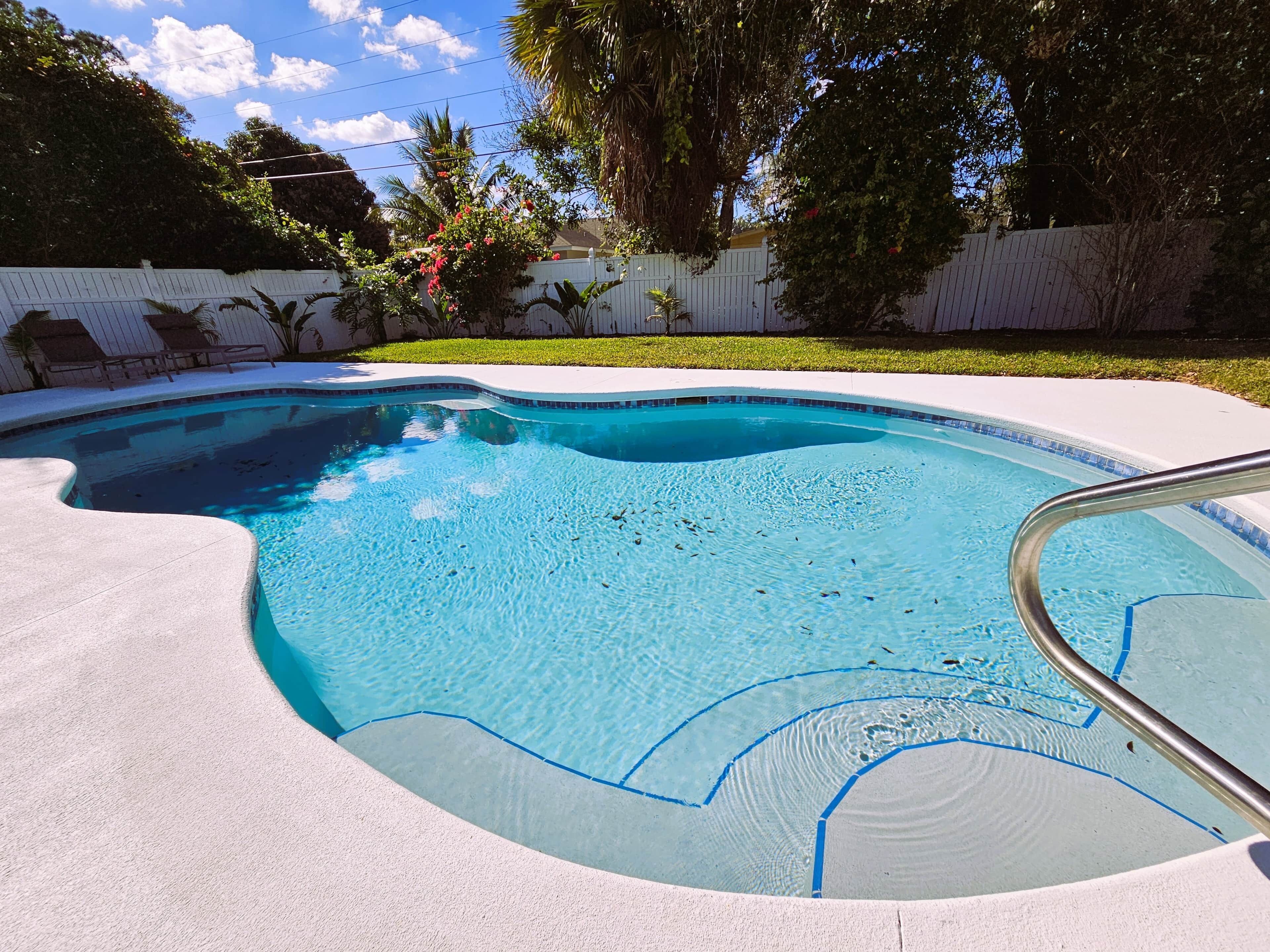 Una piscina con muelle blanco, rodeada de una cerca blanca y abundante vegetación.