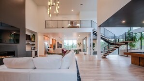 A spacious living area with a white sofa, a fireplace, and a staircase leading to an upper level. - Architectural Marvel • Pool • Pickle & Hoops (Broken Bow)