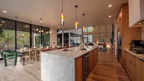 A modern kitchen with a marble island, wooden cabinets, and pendant lighting. - Architectural Marvel • Pool • Pickle & Hoops (Broken Bow)