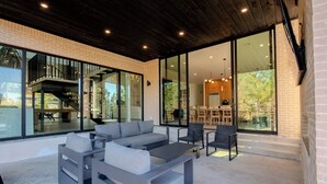 A modern outdoor seating area with a grey sofa and chairs, a coffee table, and a staircase leading to an upper level. - Architectural Marvel • Pool • Pickle & Hoops (Broken Bow)