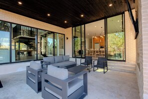 A modern outdoor seating area with a grey sofa and chairs, a coffee table, and a staircase leading to an upper level. - Architectural Marvel • Pool • Pickle & Hoops (Broken Bow)