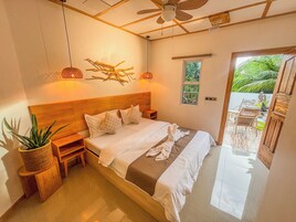 Un dormitorio con cabecera de madera, cama con ropa blanca y ventilador de techo, con vistas al exterior.