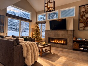 A cozy living room with a fireplace, large windows, a television, and a Christmas tree. - Snowcreek # 754 Luxury Mammoth Lakes getaway (Mammoth Lakes)